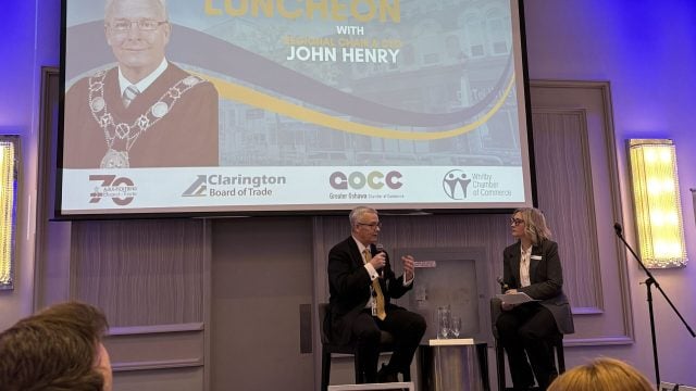 photo of fireside chat with Durham Regional Chair & CEO , John Henry interviewed by Oshawa Chamber board president Carrie-Anne Atkins, overlain with article title, Regional Chair John Henry’s Keynote: Economic Growth, Advocacy & Infrastructure